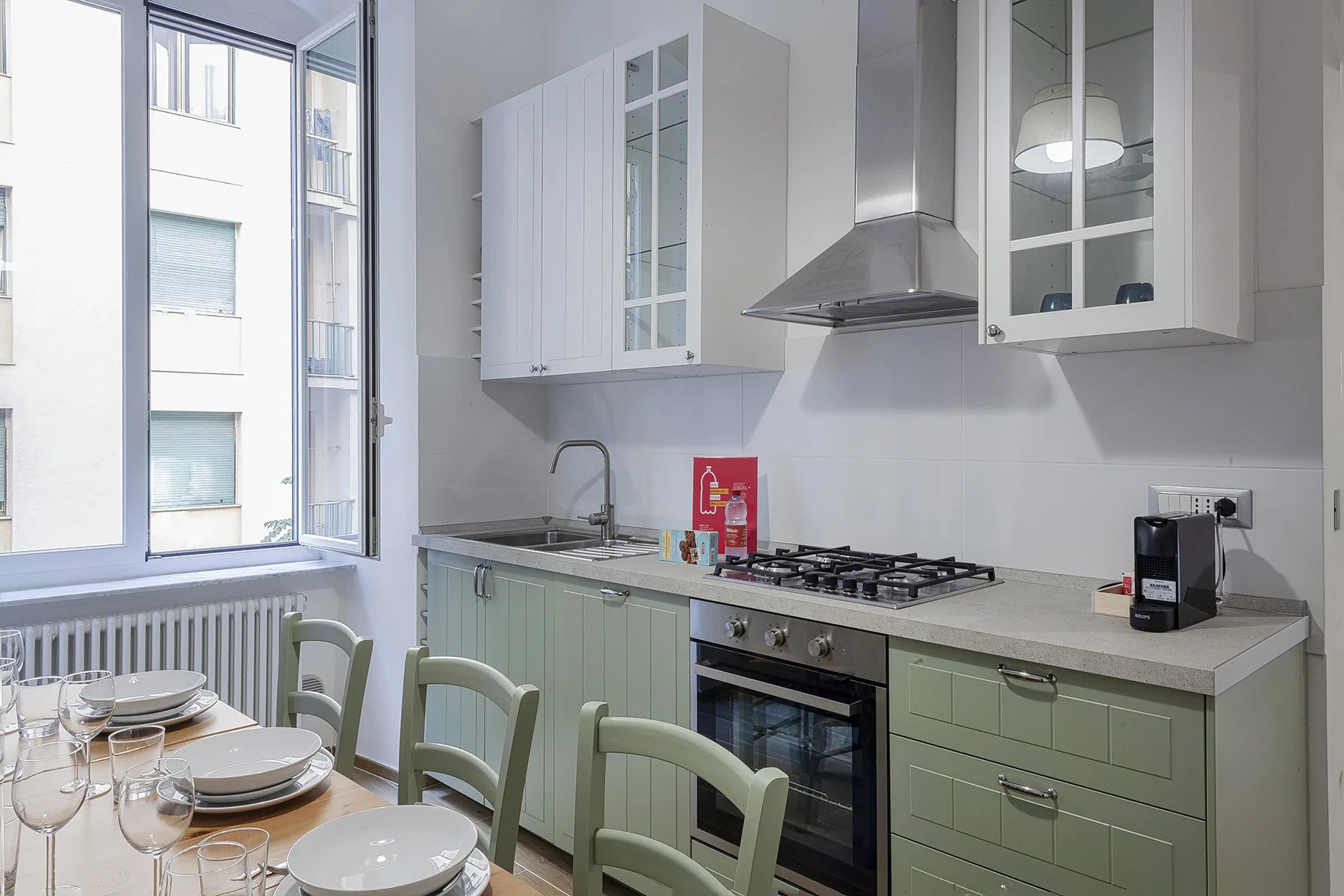 Una cocina luminosa con gabinetes verde claro, una estufa de gas y una mesa junto a la ventana.