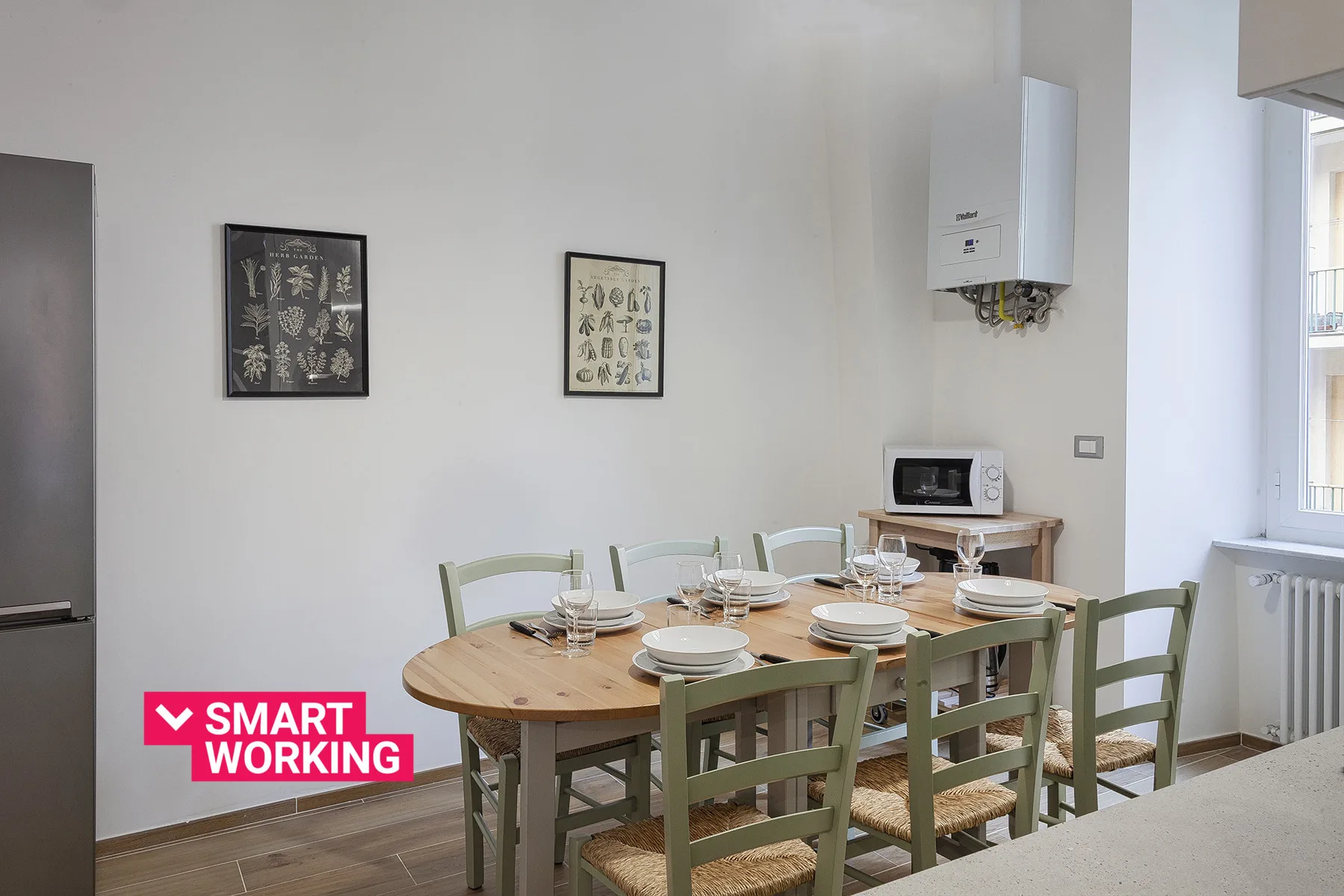 Un comedor con una mesa de madera, sillas verdes y cuadros en la pared.