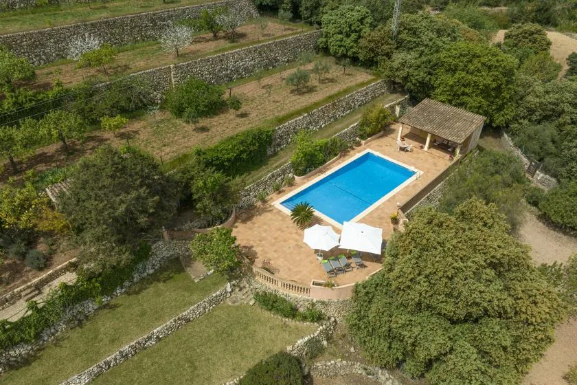 Una piscina al aire libre está junto a una terraza de piedra, rodeada de jardines verdes.