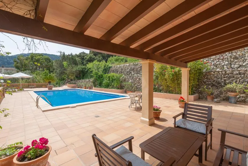 Un patio cubierto con asientos al aire libre da a una piscina y un jardín.