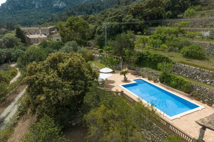 Una piscina al aire libre se encuentra entre árboles y terrazas de piedra en un paisaje montañoso.