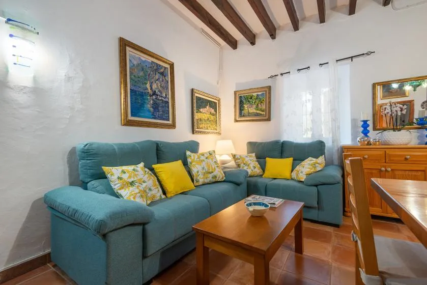 Una sala de estar con asientos color turquesa, cuadros enmarcados y una mesa de centro de madera.