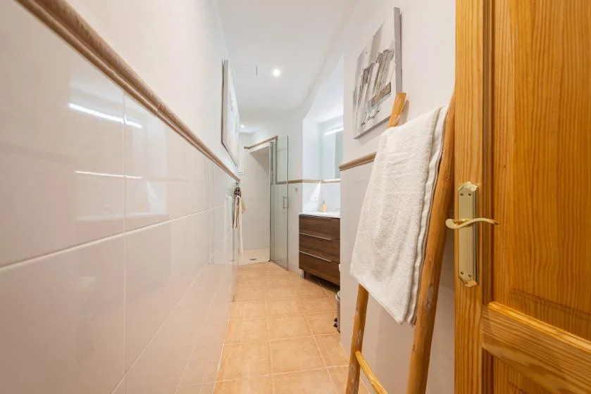 Un pasillo estrecho de baño alicatado conduce a un lavabo y un espejo.
