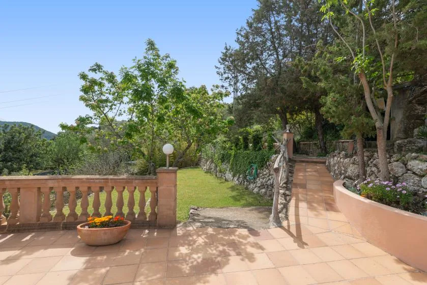 Un patio de jardín pavimentado conduce junto a un césped verde y árboles.