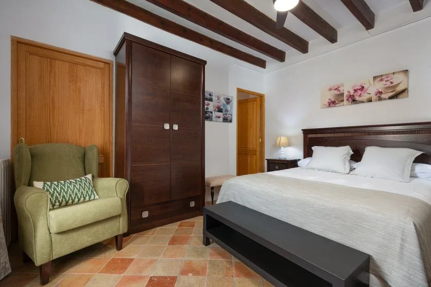 Dormitorio con una cama grande, un sillón y vigas de techo vistas.