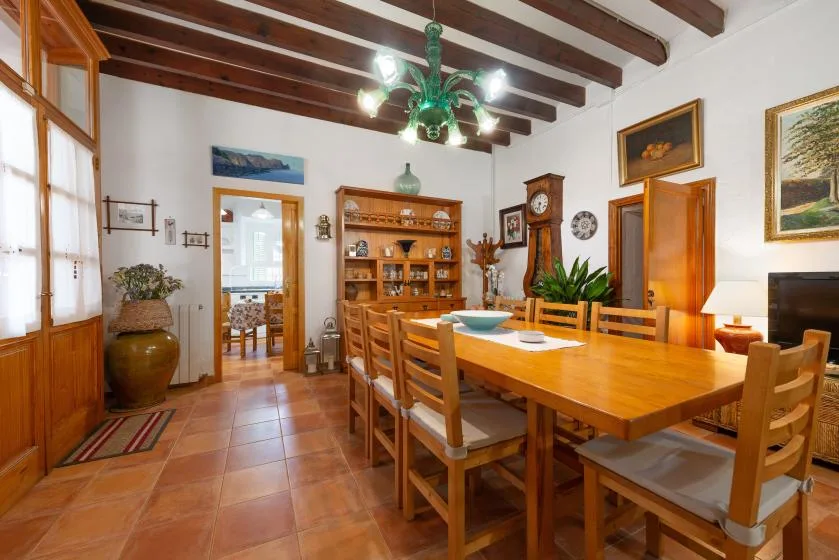 Comedor con una larga mesa de madera y sillas bajo vigas de techo vistas.