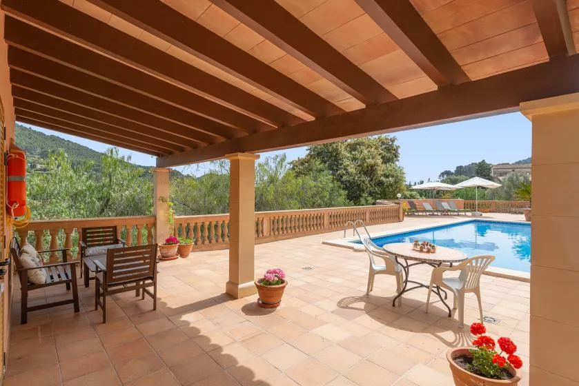 Un patio cubierto con asientos al aire libre da a una piscina y un jardín.