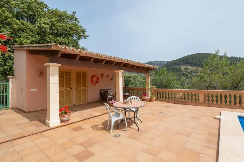 Una terraza exterior con suelo de baldosas, zona cubierta y una mesa.