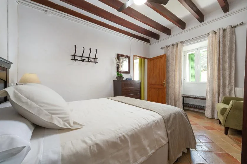 Un dormitorio con una cama bien tendida, vigas vistas y una ventana.