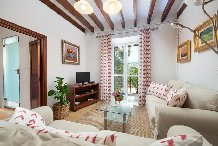 Una sala de estar con asientos color crema, una mesa de centro de vidrio y cortinas estampadas.
