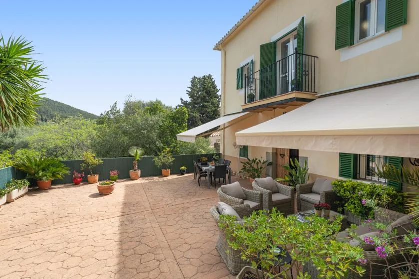 Una terraza exterior pavimentada junto a una casa, con asientos y plantas en macetas.