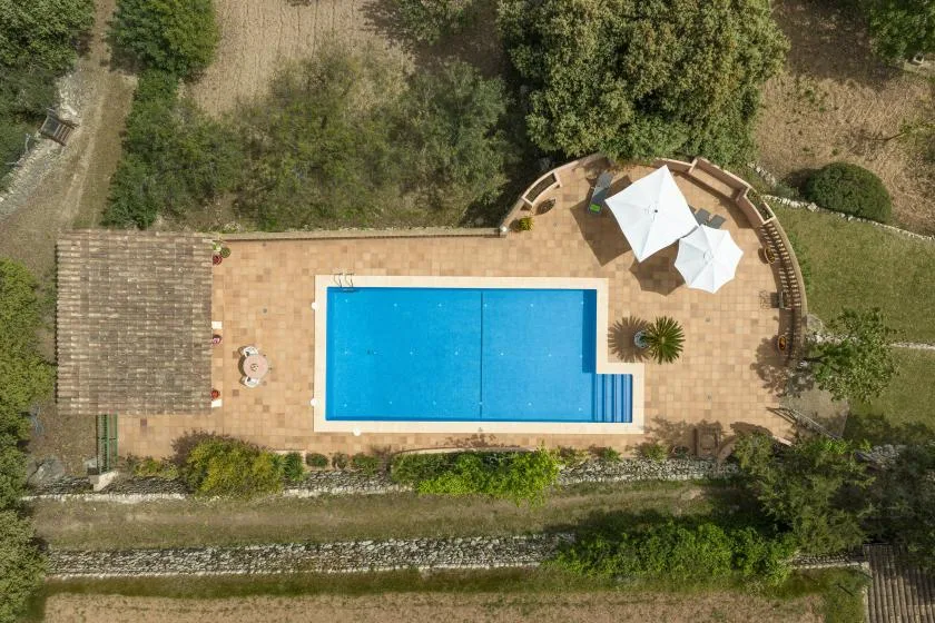 Una piscina al aire libre está junto a un patio pavimentado con sombrillas blancas.