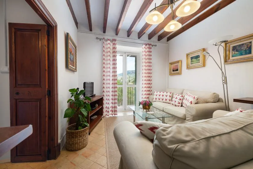 Una sala luminosa con asientos claros, una mesa de centro de vidrio y cortinas estampadas.