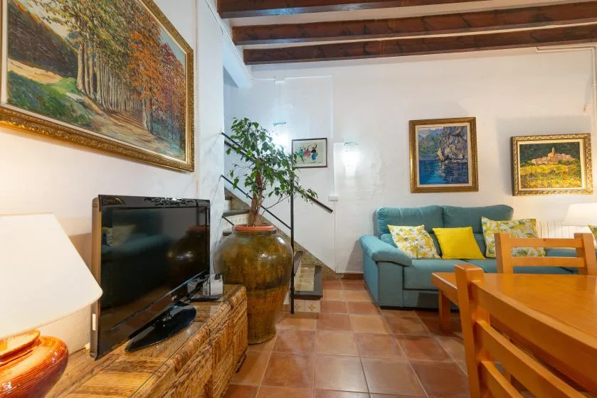 Una sala de estar con asientos color turquesa, un televisor y cuadros enmarcados.