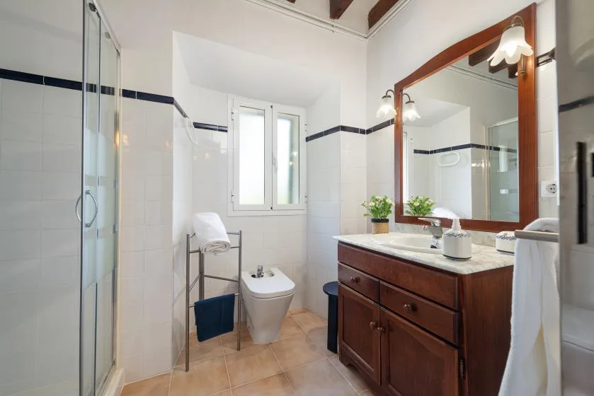 Un baño alicatado con ducha de vidrio, ventana y tocador de madera.
