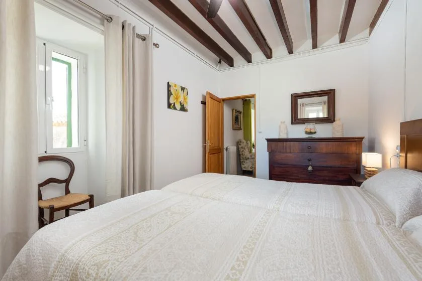 Un dormitorio luminoso con una cama bien tendida y una cómoda de madera oscura.