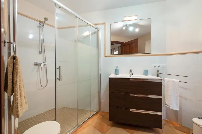 Un baño con ducha de vidrio, lavabo con mueble y espejo de pared.