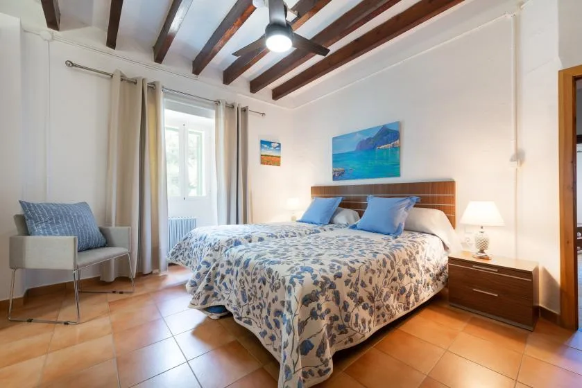 Un dormitorio con una cama doble, ropa de cama azul y una silla junto a la ventana.