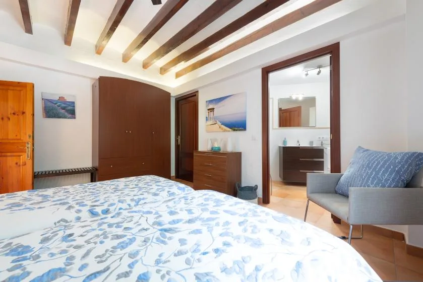 Dormitorio con ropa de cama estampada, vigas vistas y una puerta hacia el baño.