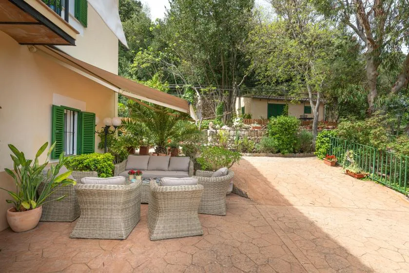 Un patio ajardinado con asientos de mimbre y plantas junto a una casa.
