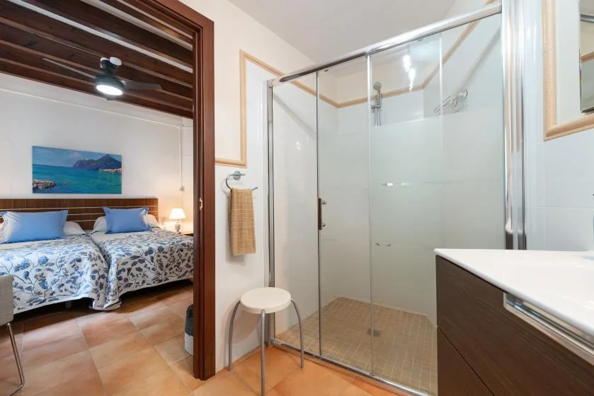 Se ve un dormitorio con dos camas junto a una ducha con paneles de vidrio.