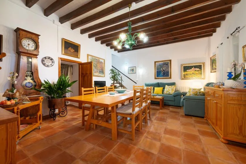 Un comedor con una mesa y sillas de madera junto a una sala con asientos verdes.