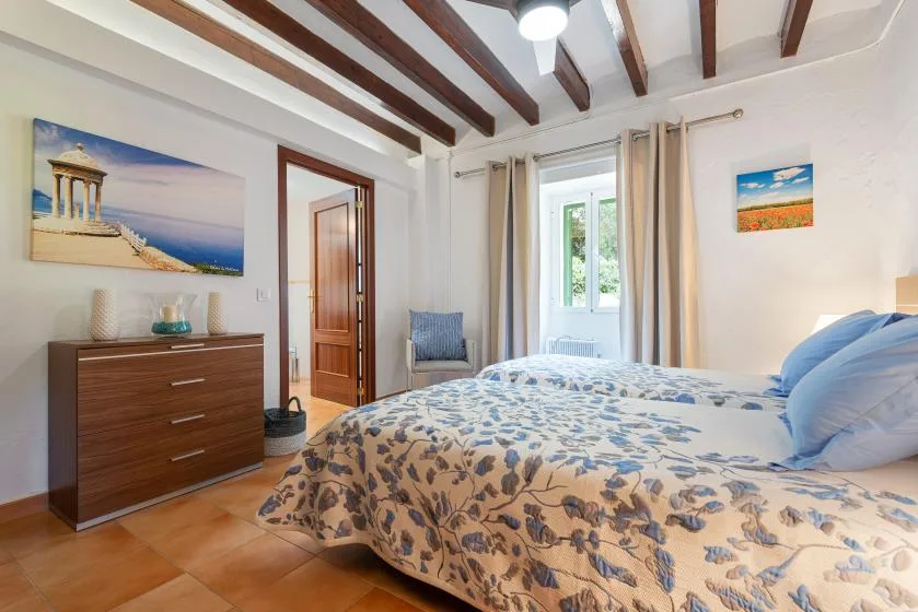 Un dormitorio con una colcha estampada, una cómoda de madera y una ventana.