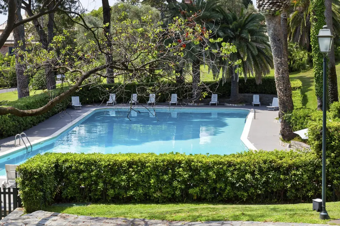 Una piscina al aire libre está rodeada de vegetación y asientos.