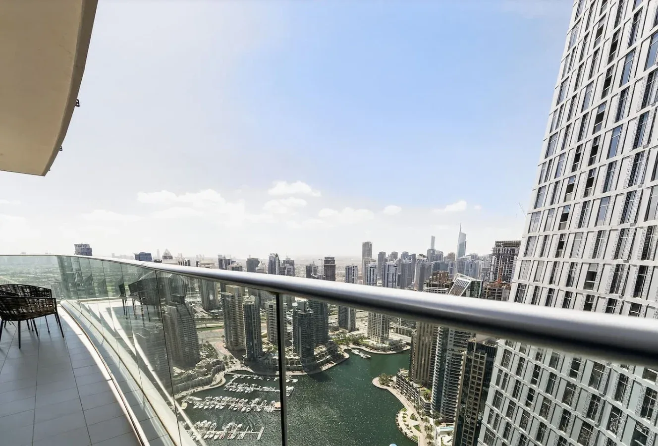 A high-rise balcony overlooks a waterfront skyline beneath a clear sky.