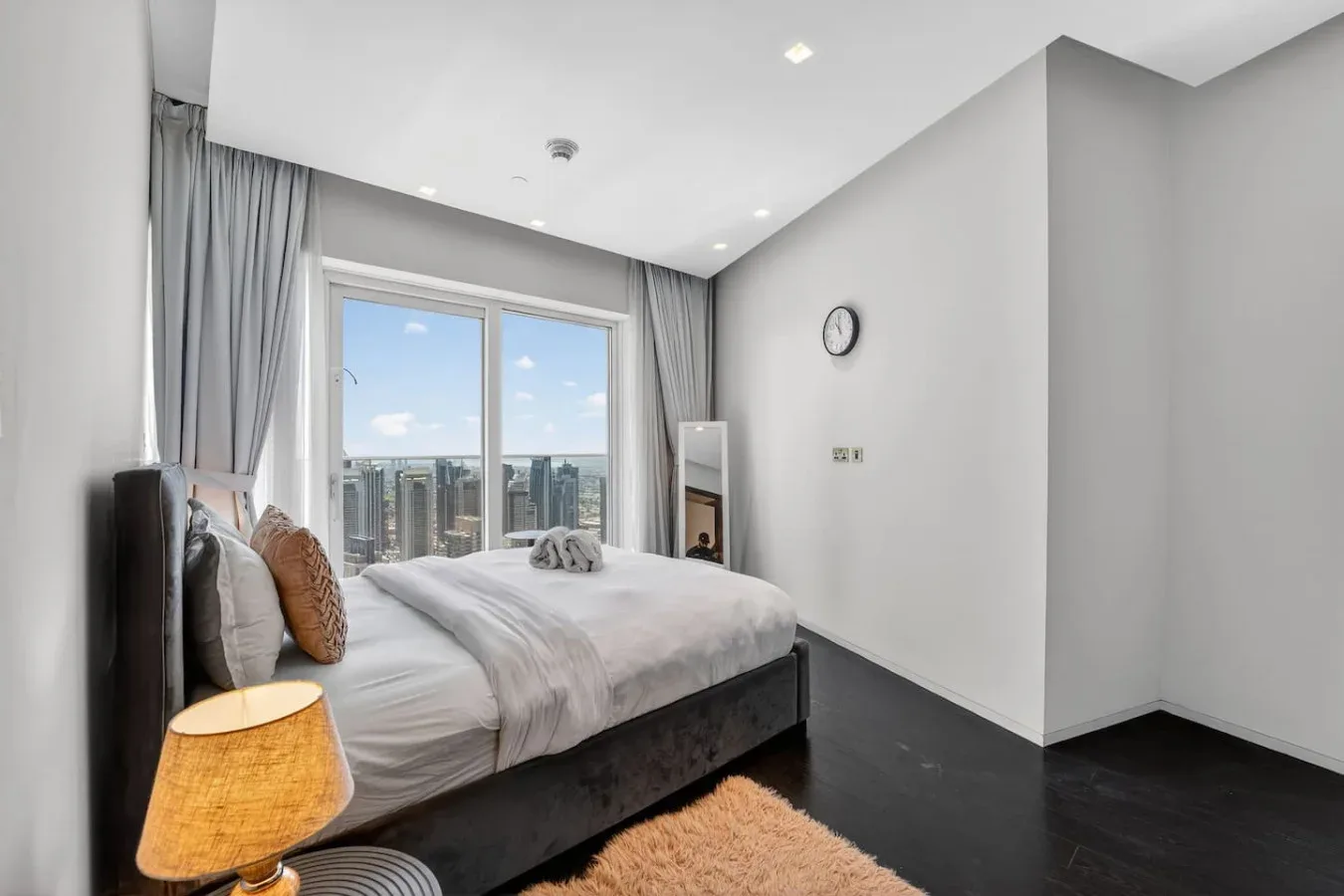 A bedroom with a bed beside a large window overlooking city buildings.