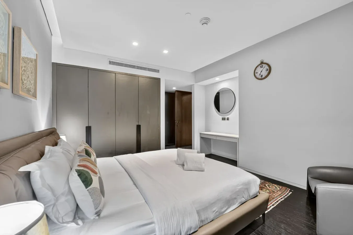 A bedroom with a neatly made bed, neutral walls, and a built-in wardrobe.