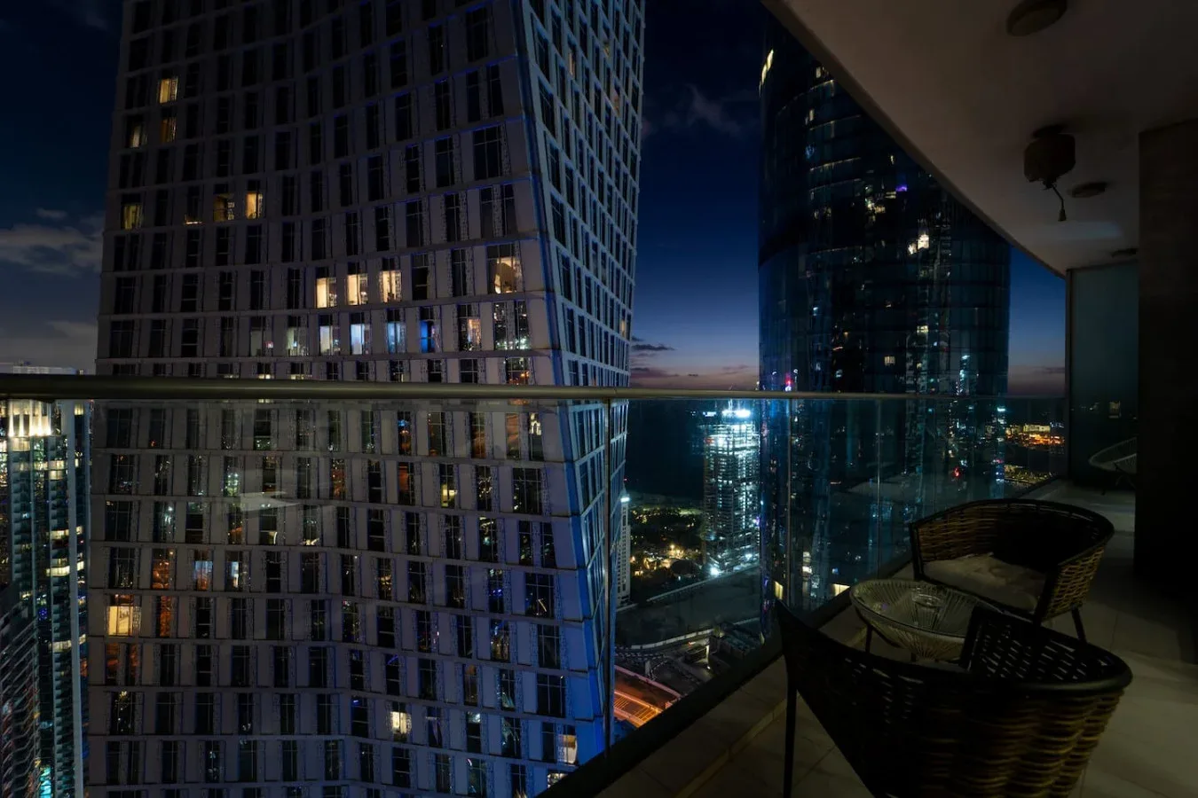 A high-rise balcony overlooks illuminated city towers at night.
