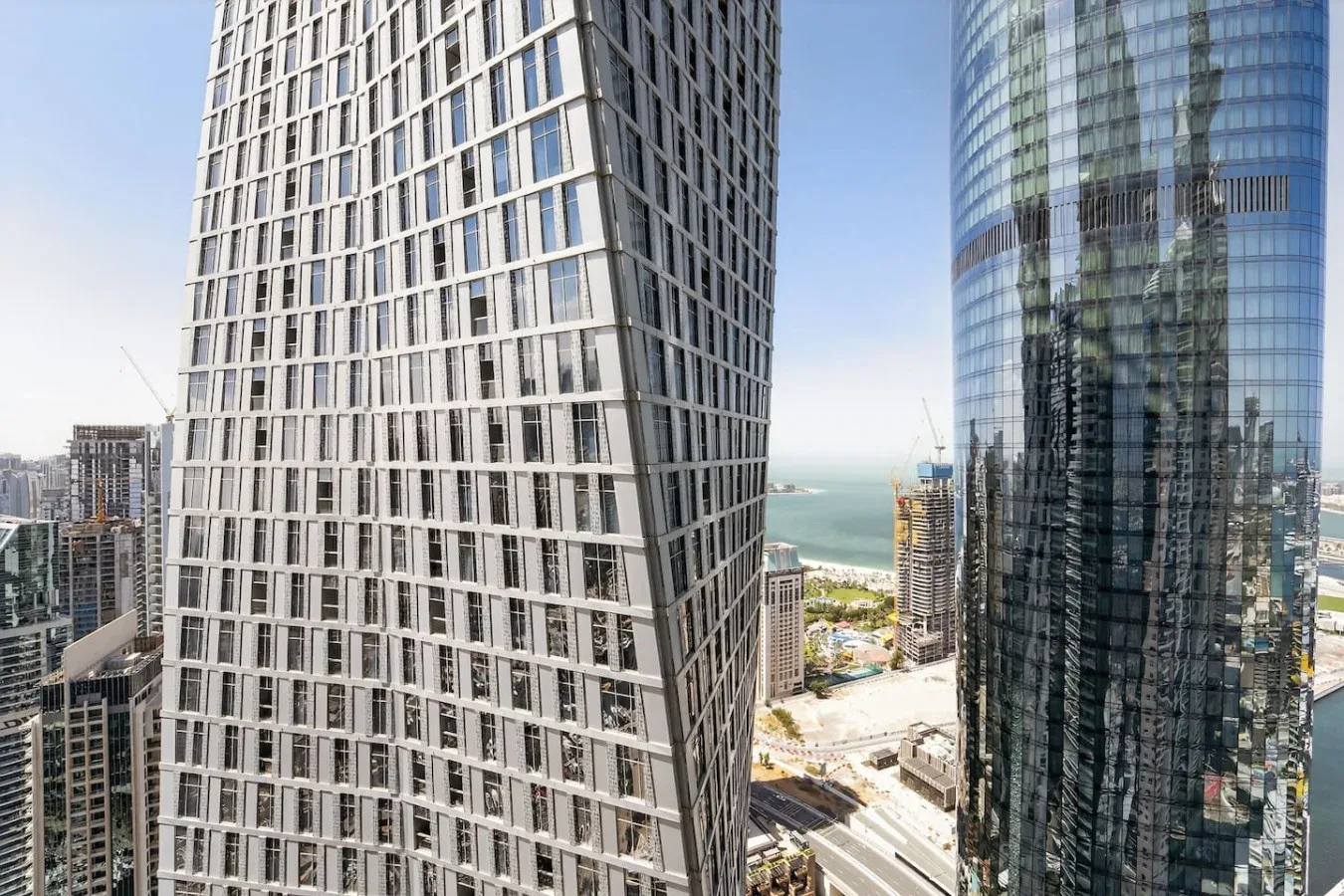 A cityscape of tall modern buildings with the water visible in the distance.