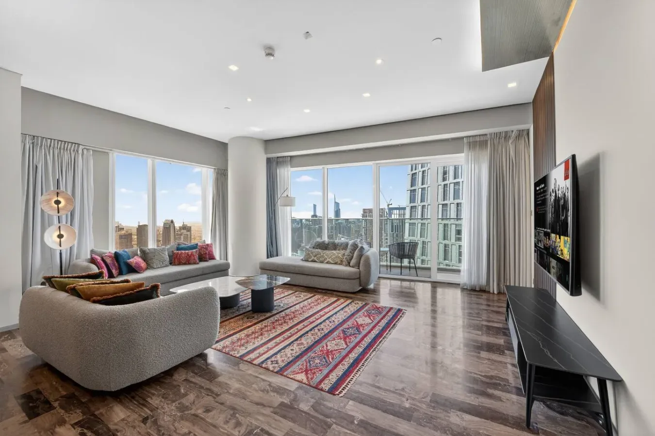 A bright living room with seating, a patterned rug, and floor-to-ceiling windows.