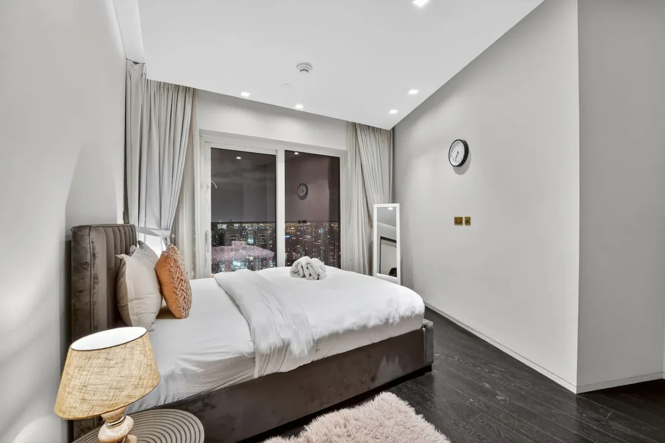 A bedroom with a bed beside a large window overlooking city lights.
