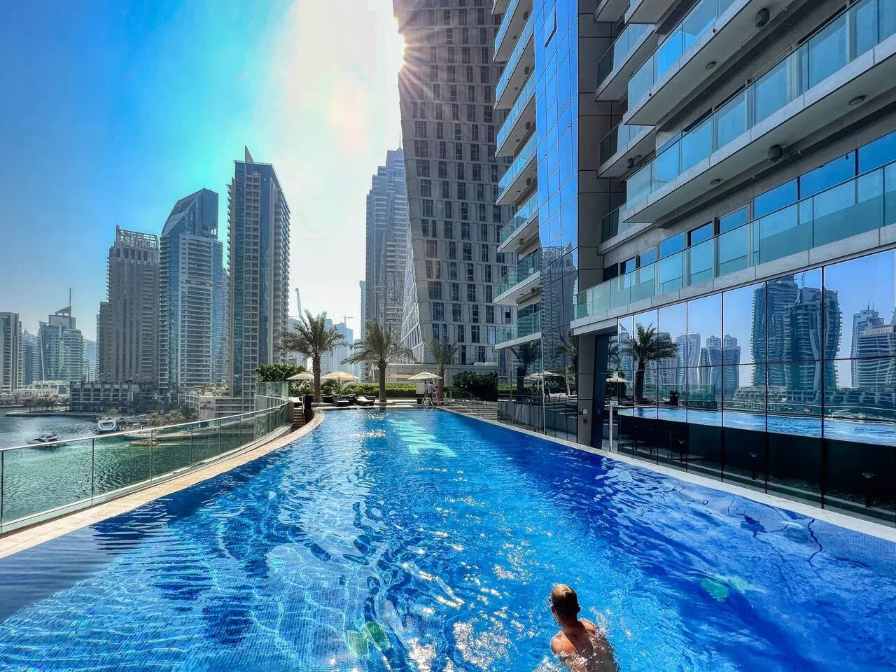 A swimming pool beside modern high-rise buildings, with a city skyline beyond.