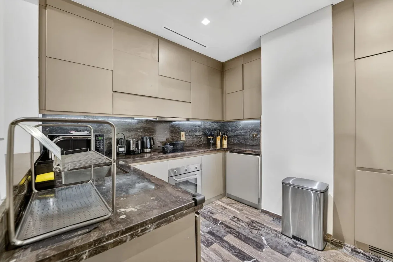 A modern kitchen with beige cabinets, stone counters, and stainless steel appliances.