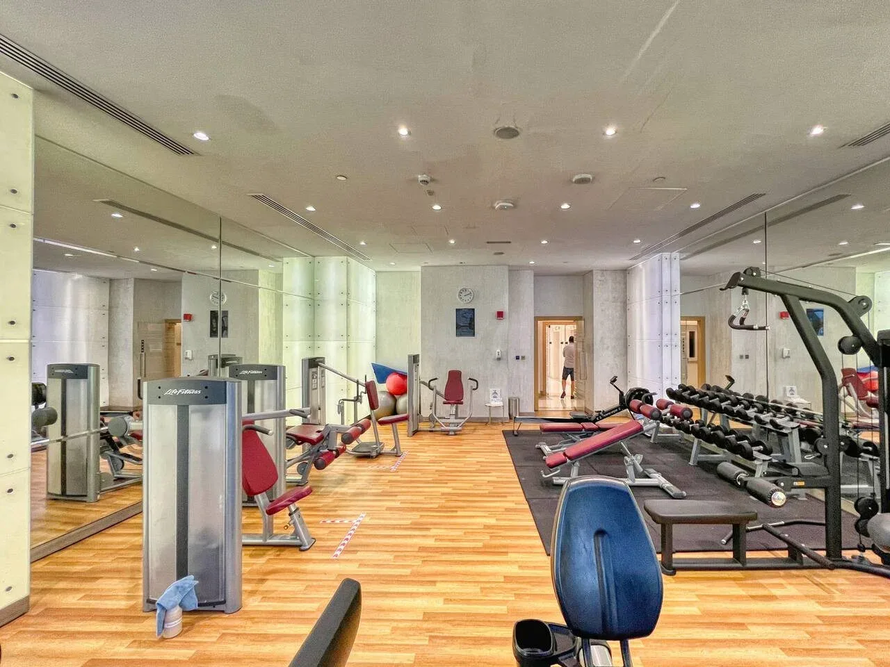 A gym with exercise machines, weights, and a wood-floored workout area.