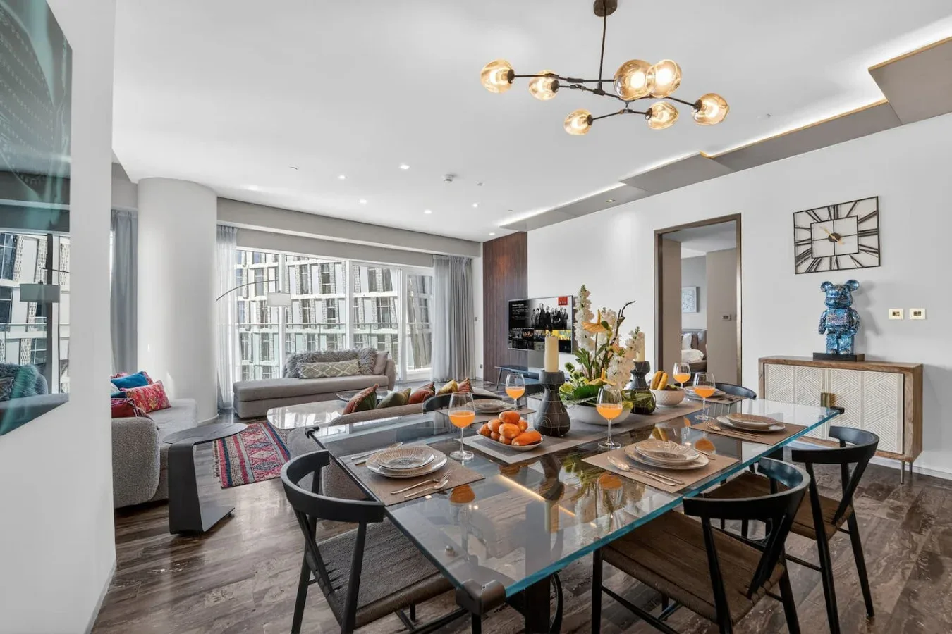 A dining area with a set table, seating, and a living area by the windows.