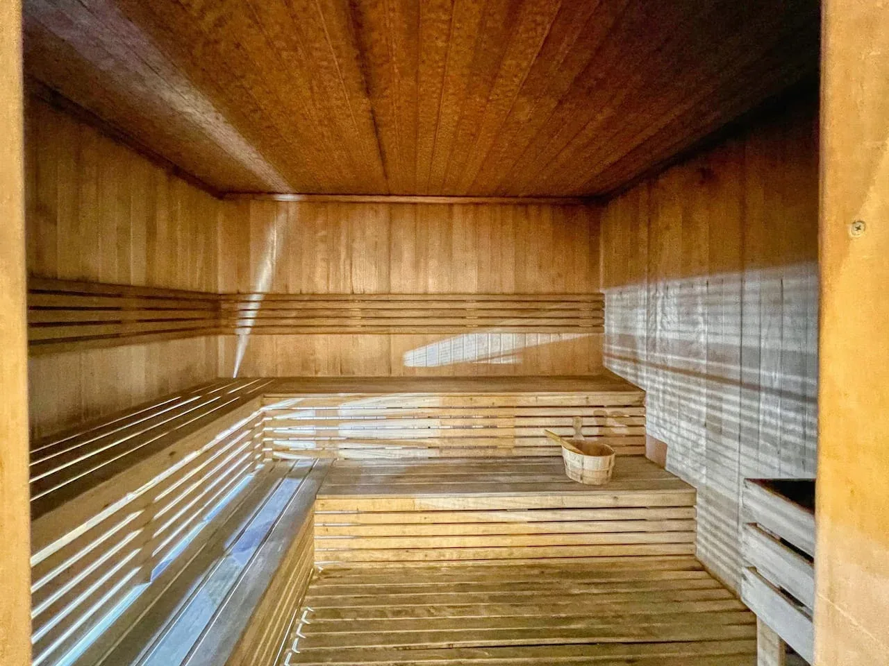 A wood-paneled sauna with tiered benches and a small bucket.