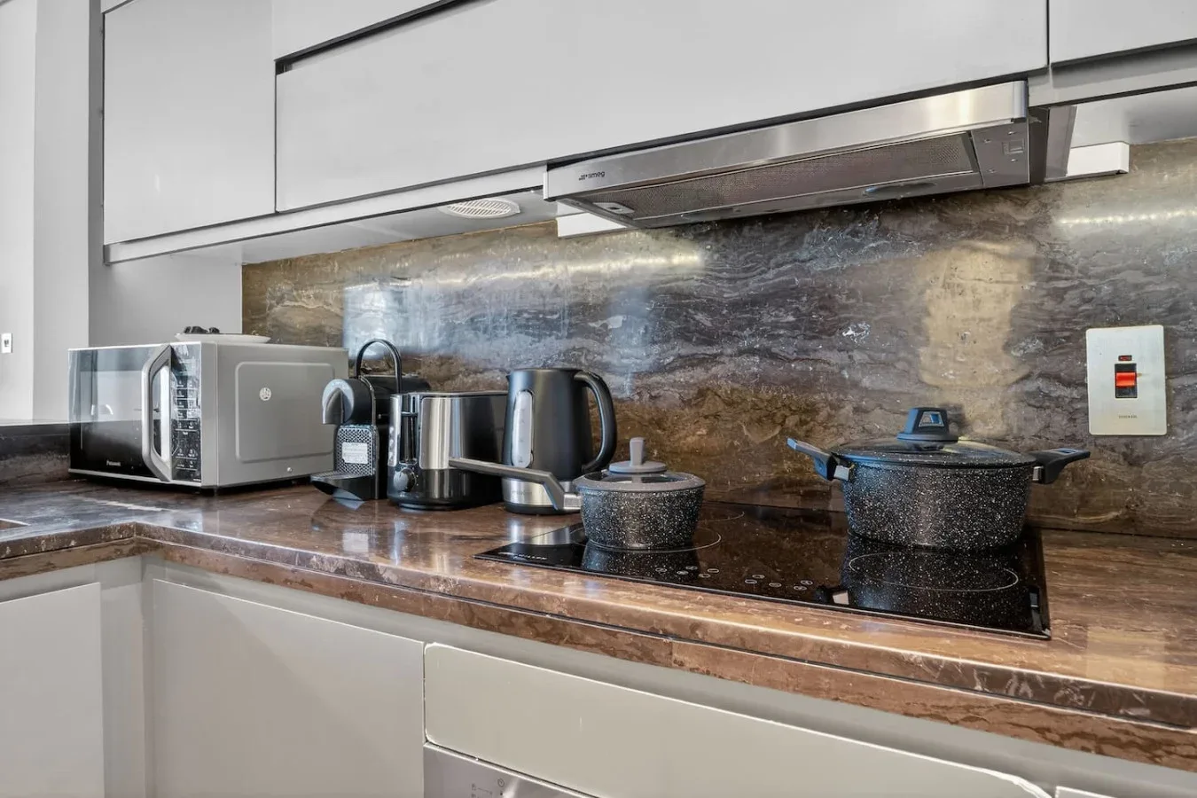 A modern kitchen counter holds small appliances and cookware beneath white cabinets.