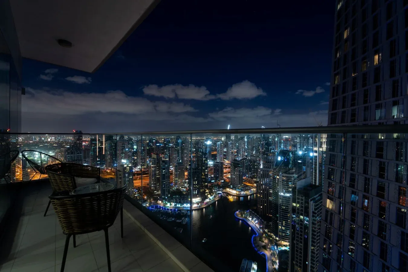 A balcony seating area overlooks a brightly lit city skyline at night.