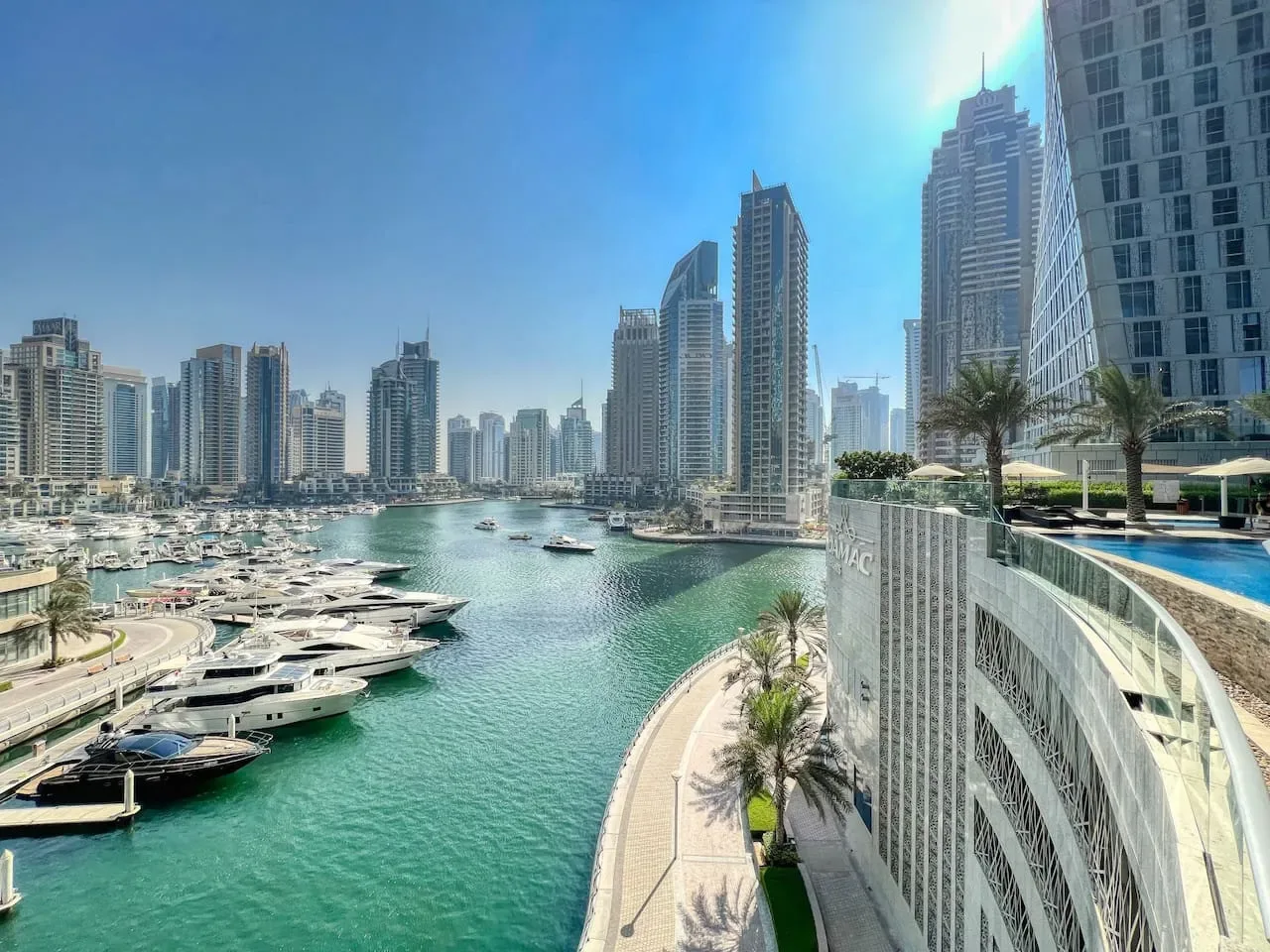 Una marina junto al agua con barcos, un paseo curvo y edificios altos.