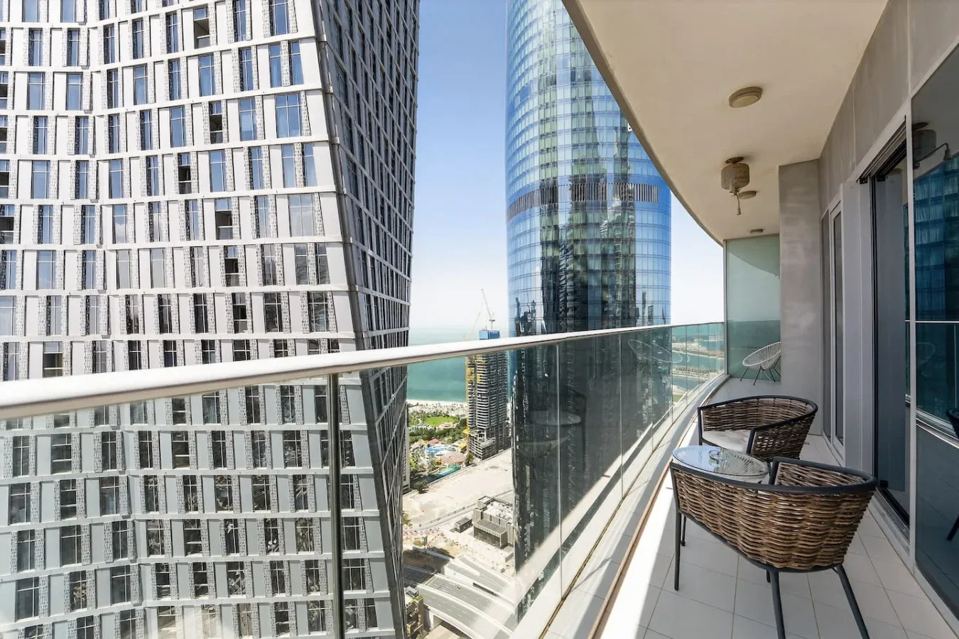 A balcony with glass railings and seating overlooks modern high-rise buildings.