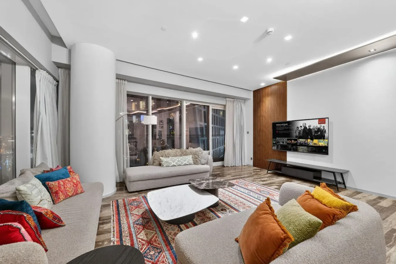 A bright living room with seating, colorful cushions, and a television.