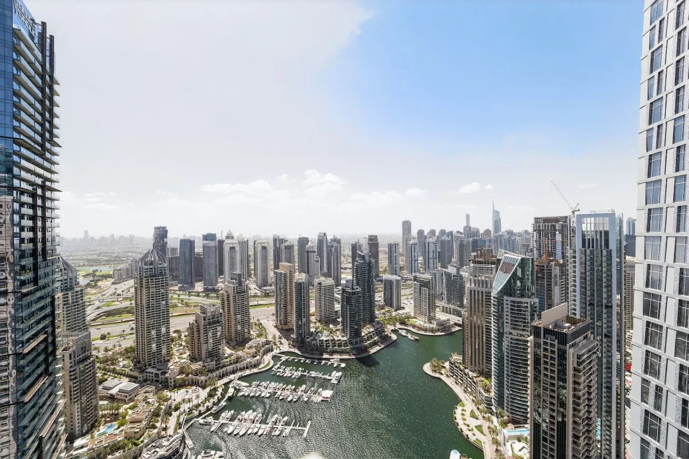 A city skyline rises around a waterfront marina beneath a clear sky.