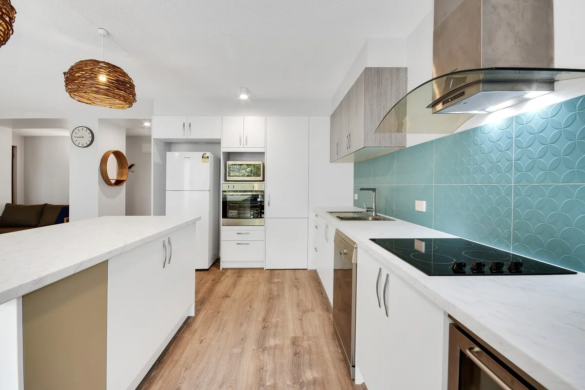Una cocina moderna y luminosa con armarios blancos y un salpicadero de azulejos turquesa.