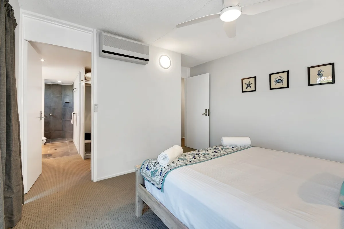 Un dormitorio luminoso con una cama bien hecha y una puerta abierta al baño.
