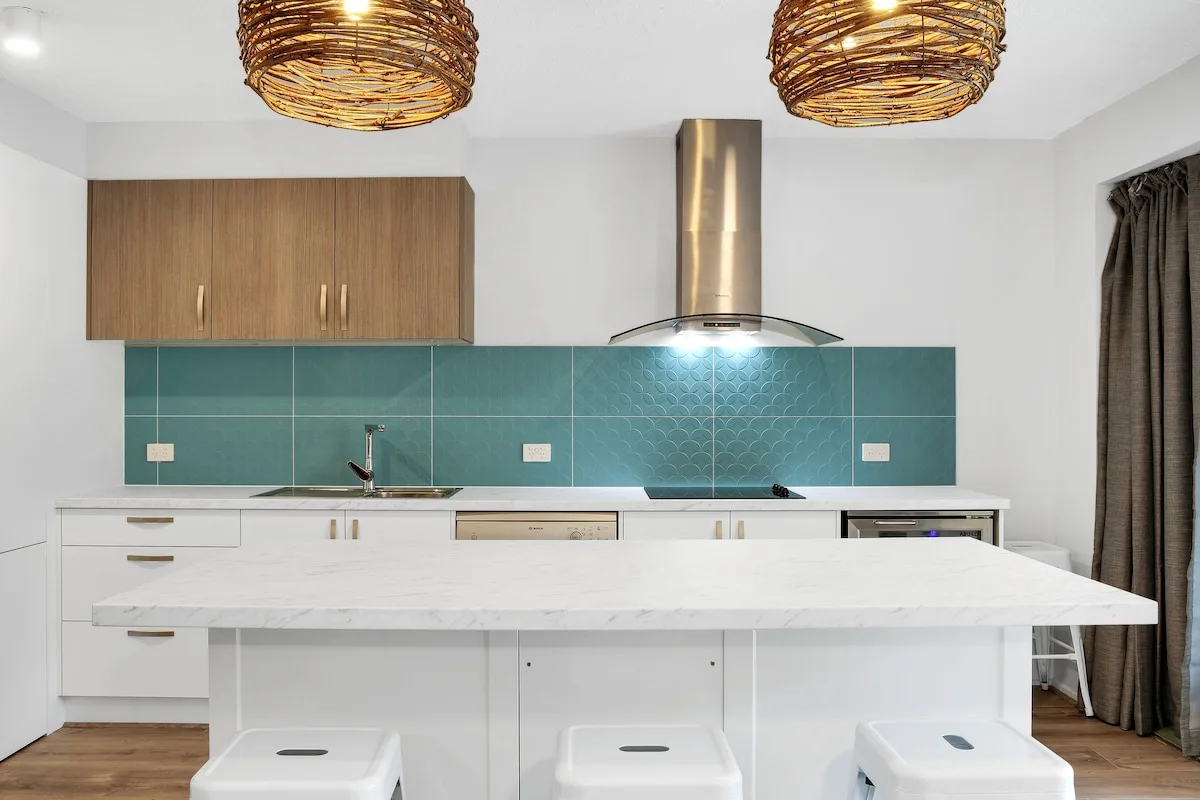 A modern kitchen with a large island, teal backsplash, and overhead pendant lights.
