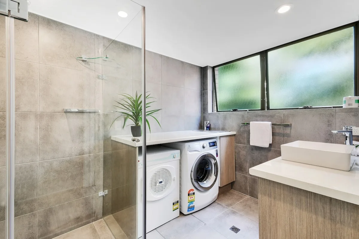 Un baño moderno con ducha, máquinas de lavandería y un lavabo sobre la encimera.